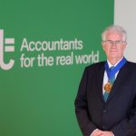 Kevin Bragg wears the Presidential medal (gold with a blue ribbon) and stands in front of a green wall with the words 'AAT Accountants for the real world' written in white.