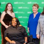 A group photo of AAT members, students and training providers standing in front of a green wall.
