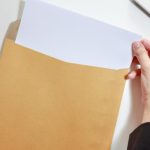 Hands pulling out a sheet of plain white paper from a brown envelope